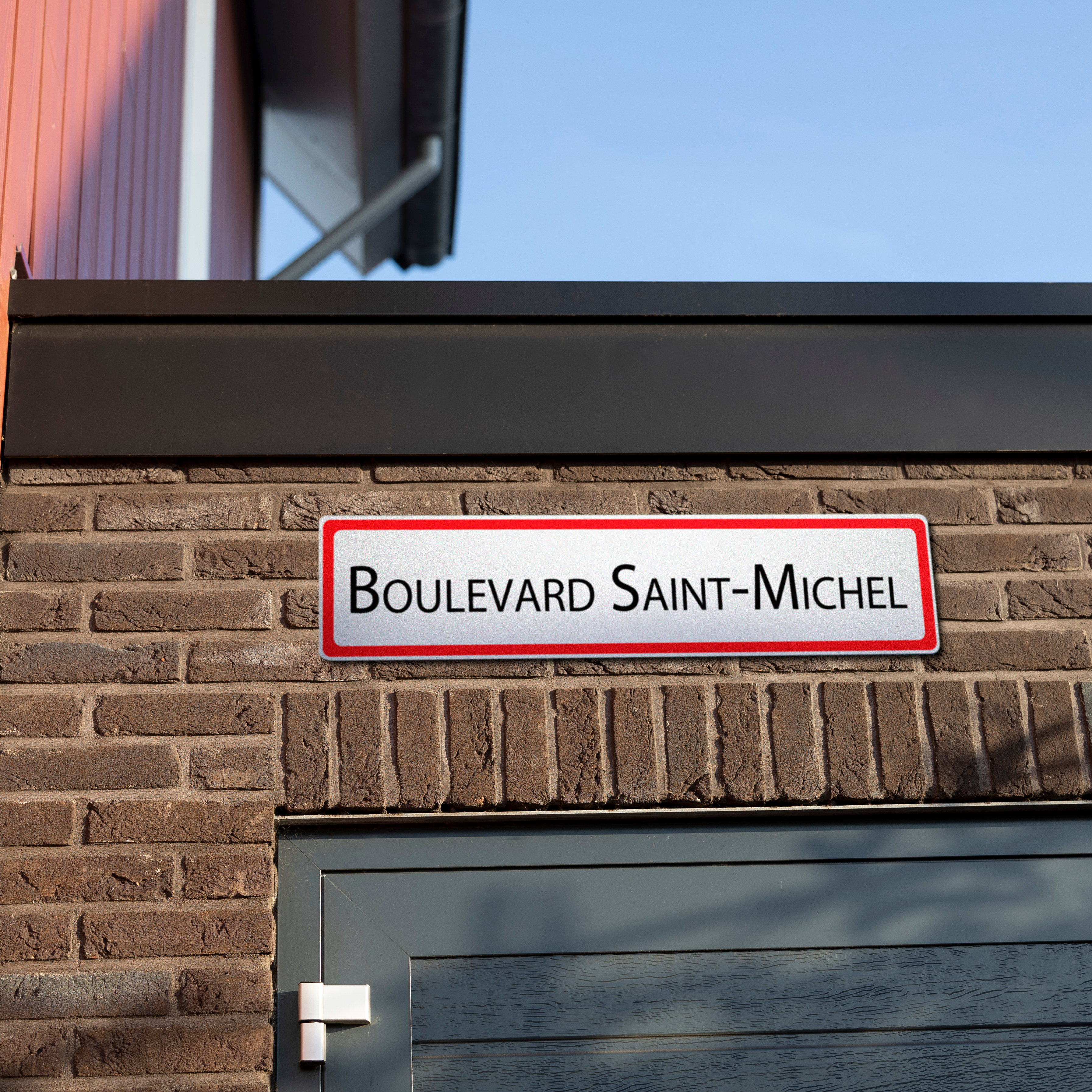 Plaque de rue personnalisée Boulevards Saint-Michel avec texte noir sur fond blanc, bordure rouge, fixée à un mur de briques.