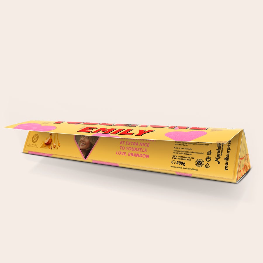 Personalizovaná Toblerone - Láska Personalizovaná Toblerone čokoláda s fotkou usmievajúcej sa ženy a textom "EMILY" na obale, s odkazom "BE EXTRA NICE TO YOURSELF. LOVE, BRANDON" na boku.