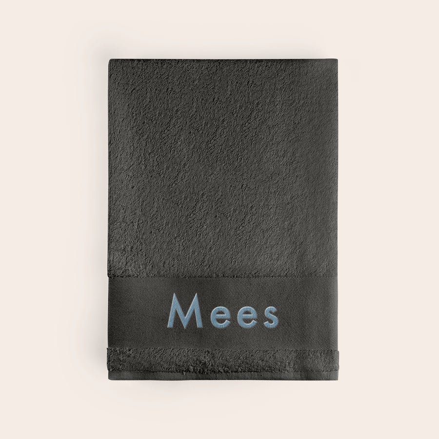 Badlaken met naam Zwart badlaken met naam "Mees" erop geborduurd in lichtblauw garen, voor een badlaken met naam.