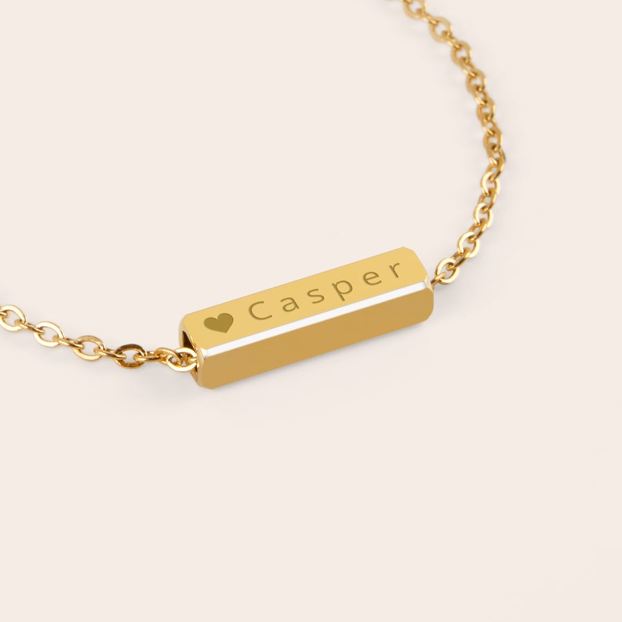 Náramek se štítkem na jméno Personalizovaný náramek ve zlaté barvě se jménem "Casper" a srdíčkem gravírovaný na destičce.