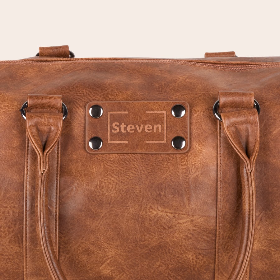 Geanta de weekend personalizata din piele PU Geantă de weekend maro din piele PU, personalizată cu numele Steven gravat central pe o placă metalică decorativă. Călătorește cu stil cu această geantă personalizată de weekend din piele PU gravată cu un nume sau un text.