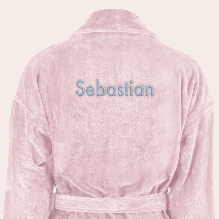 Badrock Herr med namn En mjuk, ljusrosa morgonrock med "Sebastian" broderat i ljusblått på ryggen.