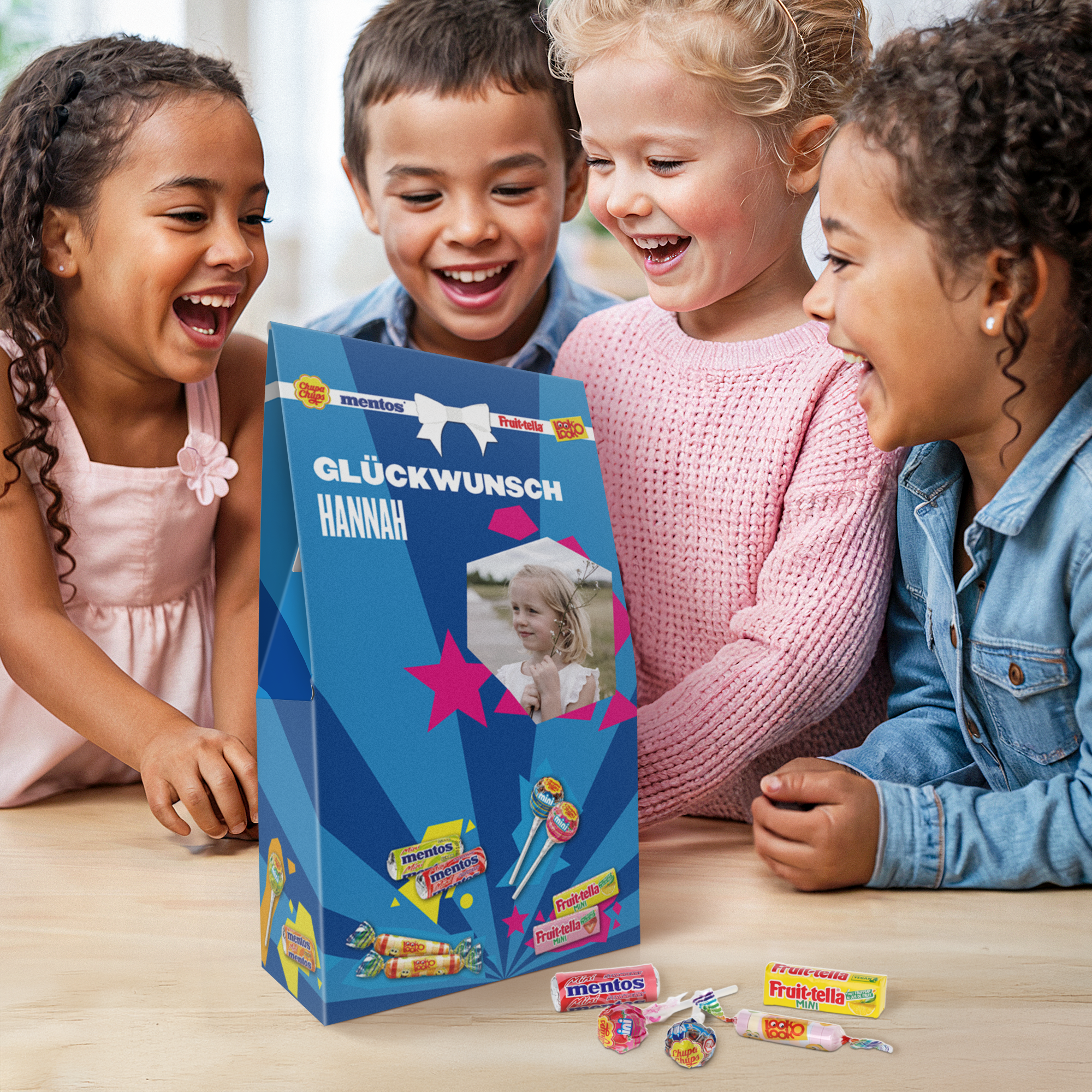 Personalisierte Fruit-tella Bonbonmischung mit Foto und dem Namen Hannah, auf blauem Karton gedruckt, umgeben von lachenden Kindern.