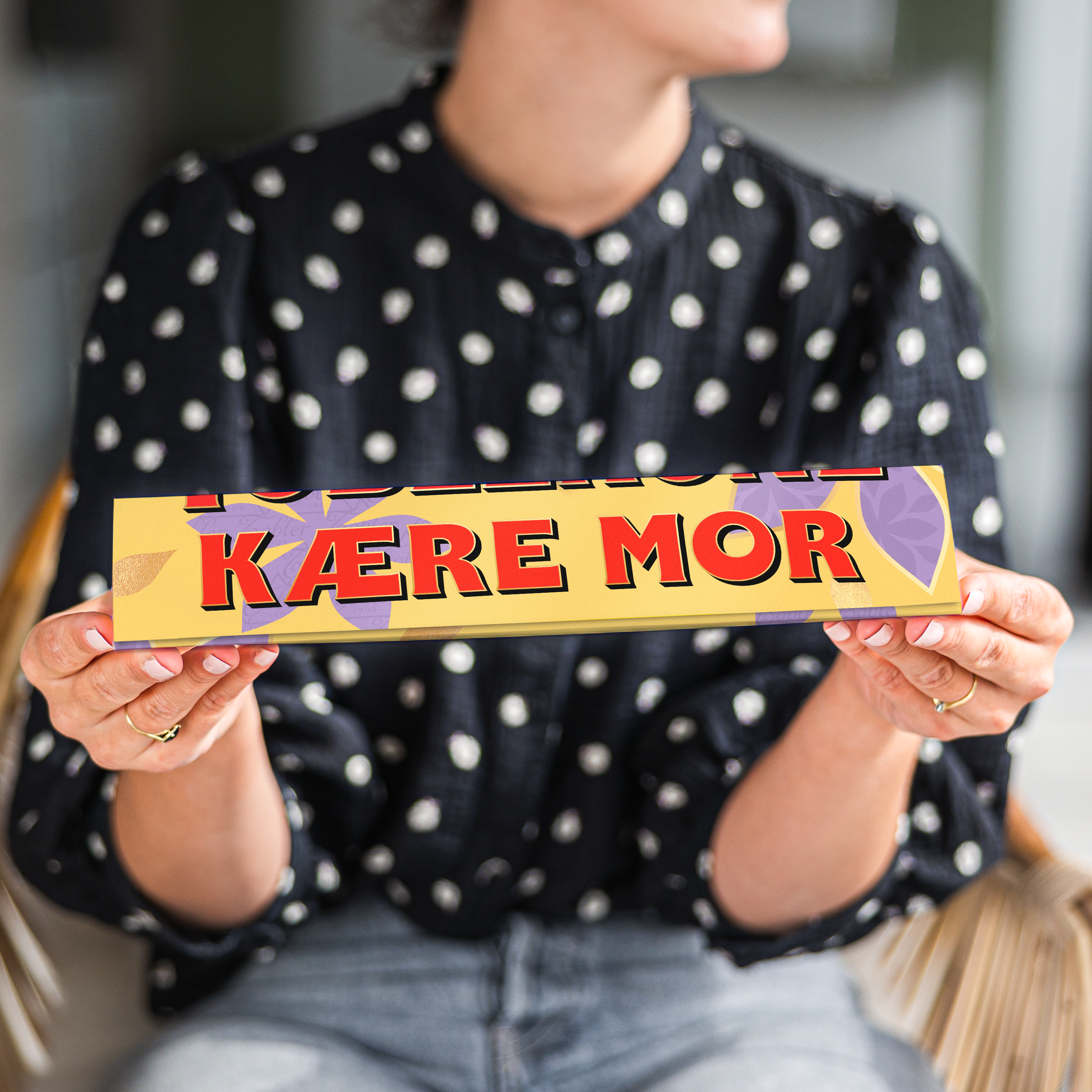Personlig Toblerone chokoladebar med teksten KÆRE MOR trykt på indpakningen, holdt af en kvinde. Overrask din mor med en unik chokoladegave.