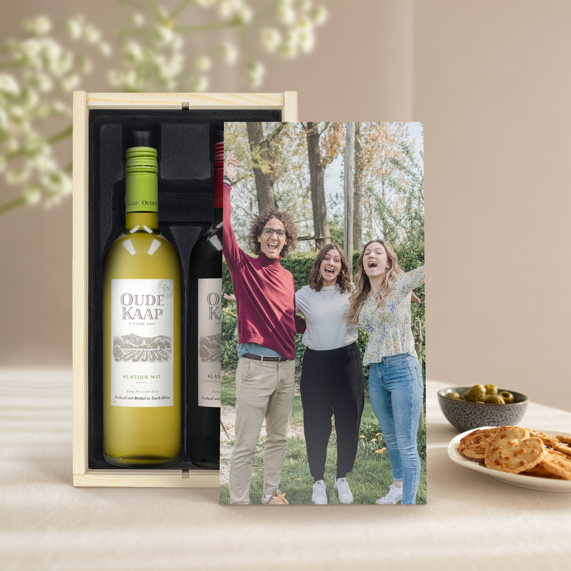 Duas garrafas de vinho Oude Kaap (branco e tinto) numa caixa de madeira impressa com uma foto personalizada de três pessoas sorrindo.