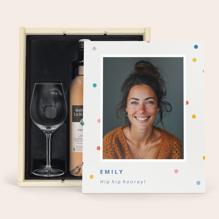 Maison de la Surprise Syrah Fa díszdoboz személyre szabott boros készlettel, egy üveg Maison de la Surprise rosé borral és egy gravírozott borospohárral, mellette egy polaroid fotó Emilyről.