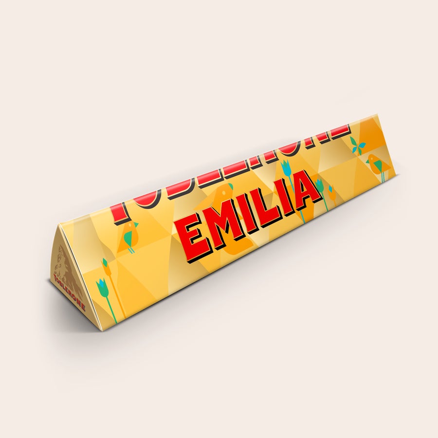 Toblerone med namn En personaliserad Toblerone med namnet Emilia tryckt i rött på ett färgglatt omslag.