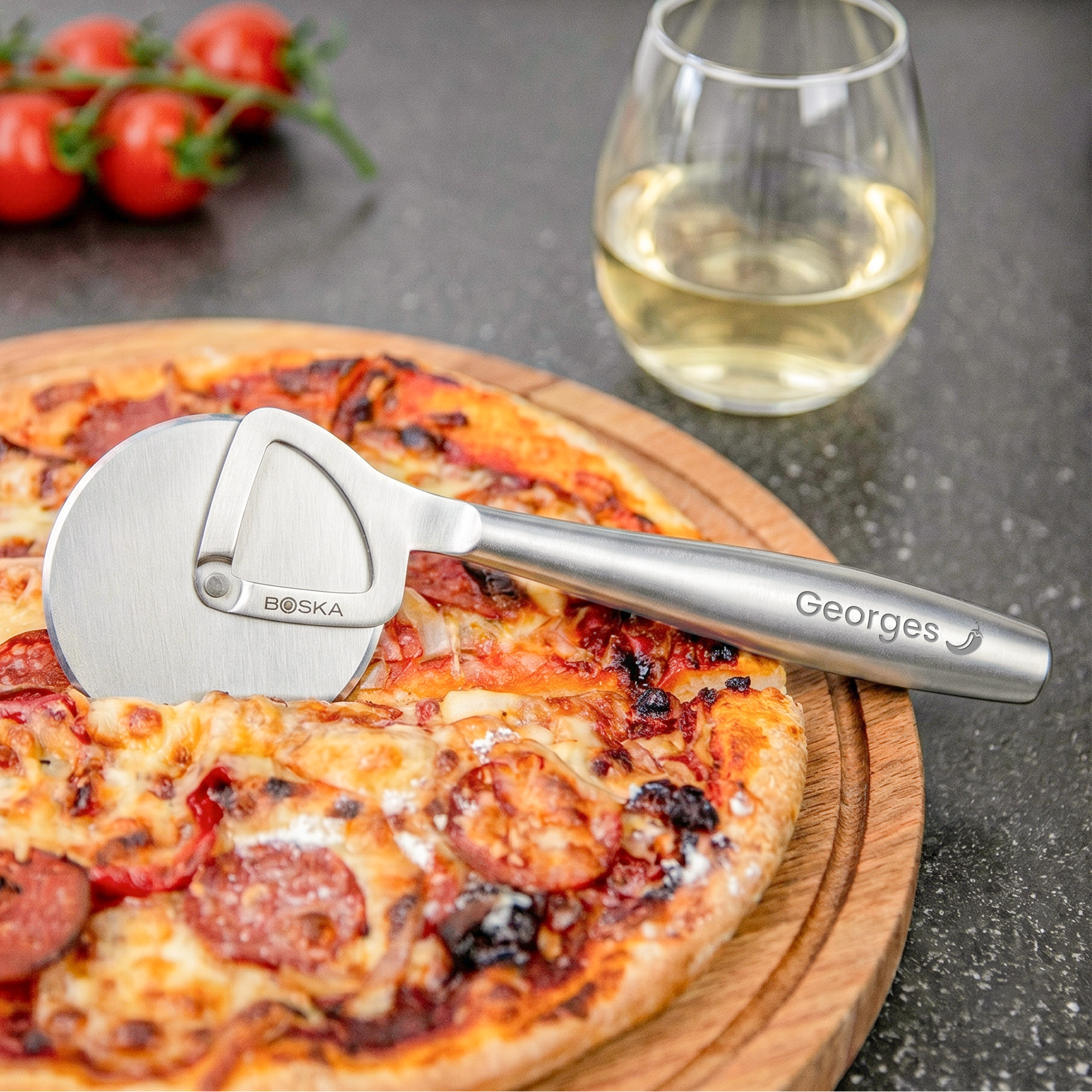 Roulette à pizza personnalisée BOSKA en acier inoxydable avec nom Georges gravé, posée sur une pizza appétissante et une planche en bois.