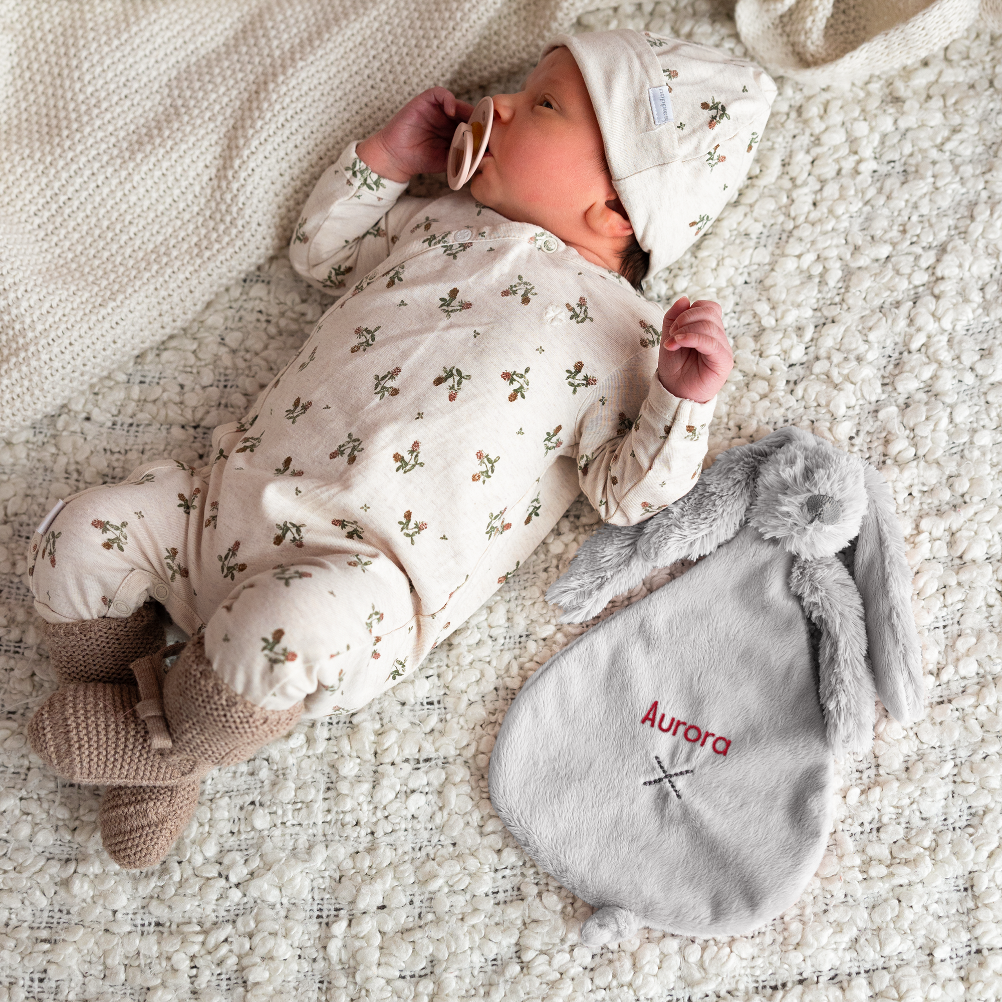 Kosekanin fra Rabbit Richie i grått, brodert med navnet Aurora i rødt ved siden av en baby.