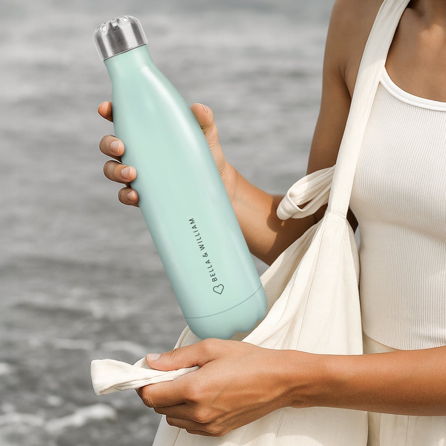 Personalised insulated water bottle A person holding a mint-green personalised Thermos bottle printed with "BELLA & WILLIAM" and a heart graphic.