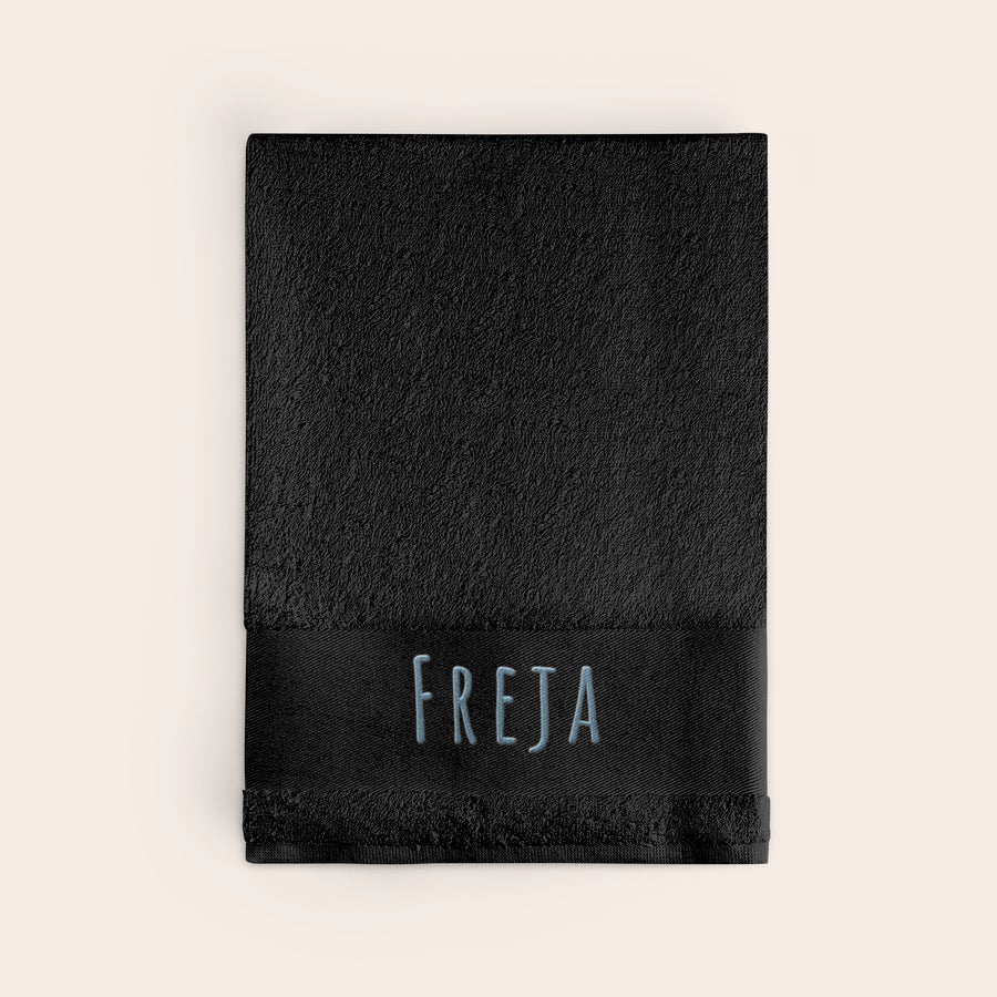 Badhandduk med text Svart personaliserad badhandduk med namnet FREJA broderat i blå tråd, en unik design