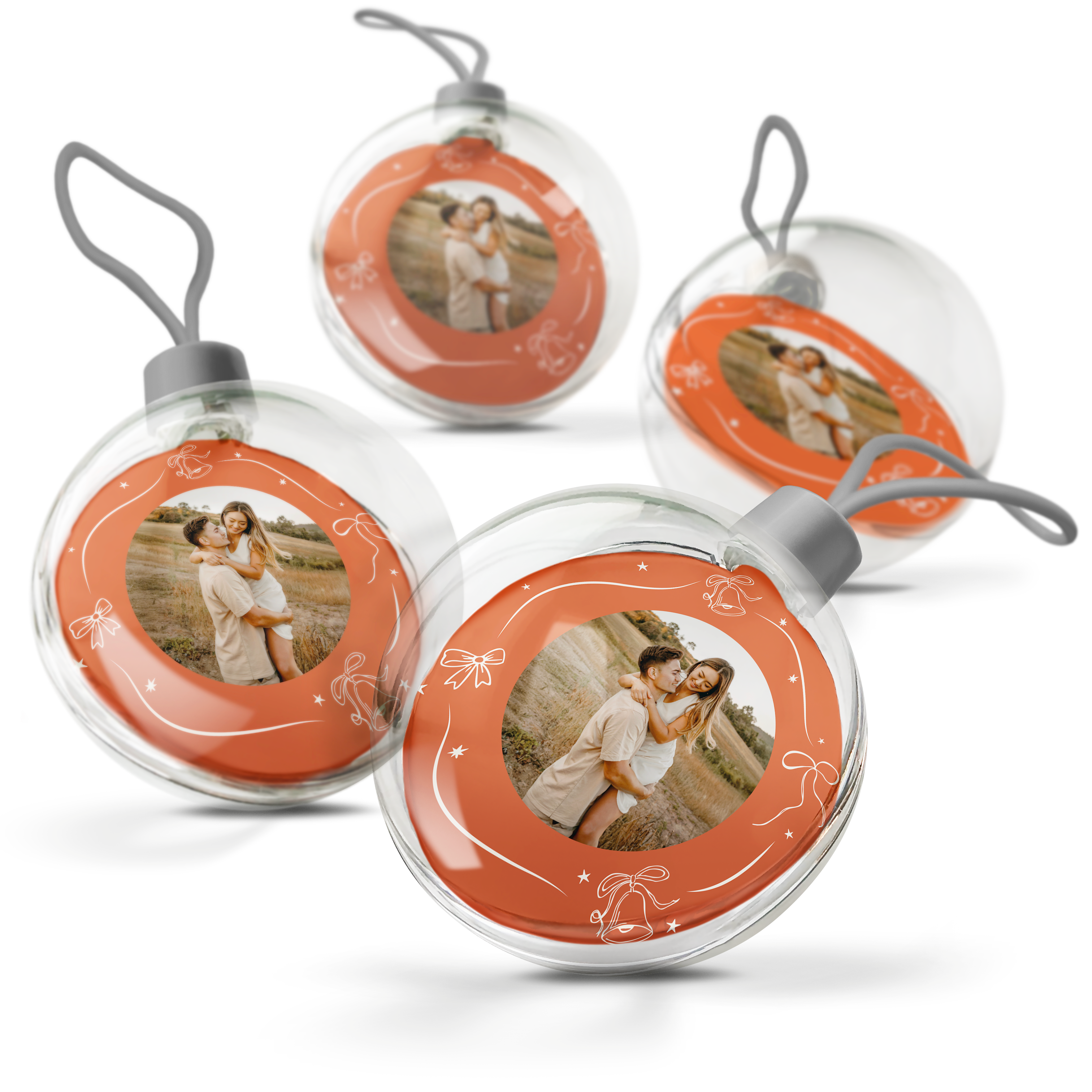 Vier transparante kerstballen met een oranje accent en daarin een geprinte foto van een stel, gedecoreerd met witte feestelijke tekeningen.