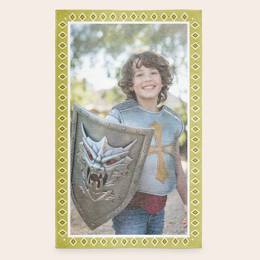 Speelkleed bedrukken Gepersonaliseerd speelkleed met foto van lachende jongen in ridderpak, omrand door een geel patroon.