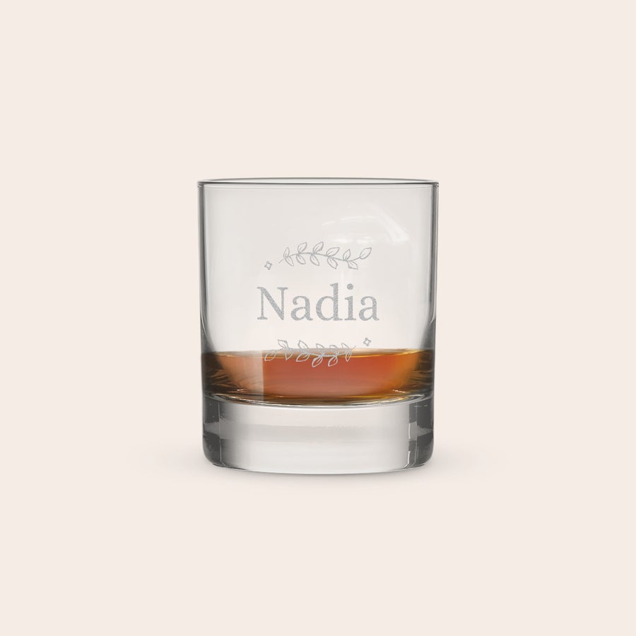 Graveret Whiskyglas Personligt whiskyglas indgraveret med navnet Nadia og et detaljeret blomstermønster, fyldt med mørk væske.