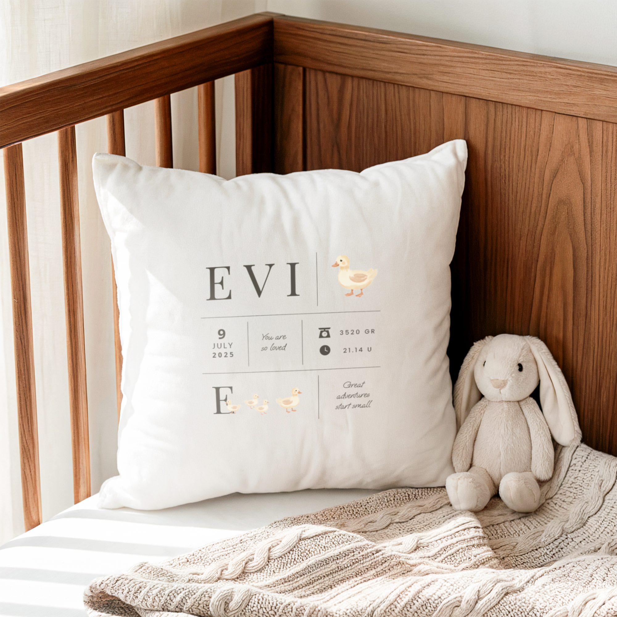 White birth cushion with name EVI, birth date 9 July 2025, weight 3520 GR, and time 21:14 U, printed with cute ducks, sitting in a wooden cot next to a bunny plush toy.