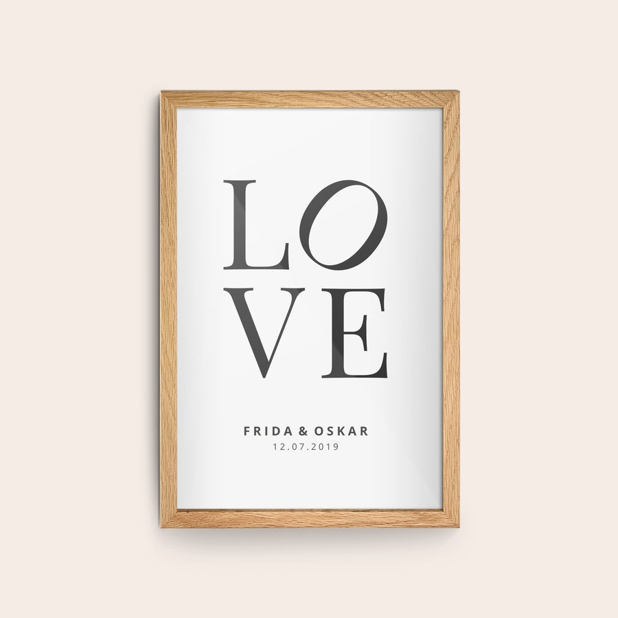 Innrammet bilde Personlig plakat med trykt LOVE-motiv, navnene Frida & Oskar og datoen 12.07.2019 i en treramme.