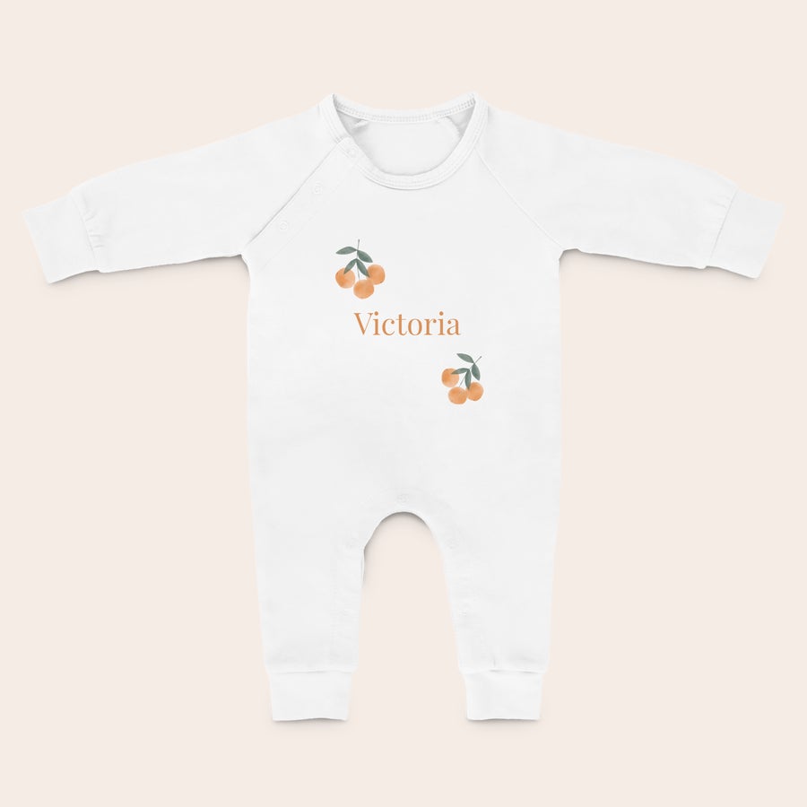 Babystrampler bedrucken Weißer Babystrampler mit langen Ärmeln bedruckt mit dem Namen "Victoria" und kleinen orangefarbenen Früchten. Dieser Babystrampler ist eine tolle Überraschung für die frischgebackenen Eltern.