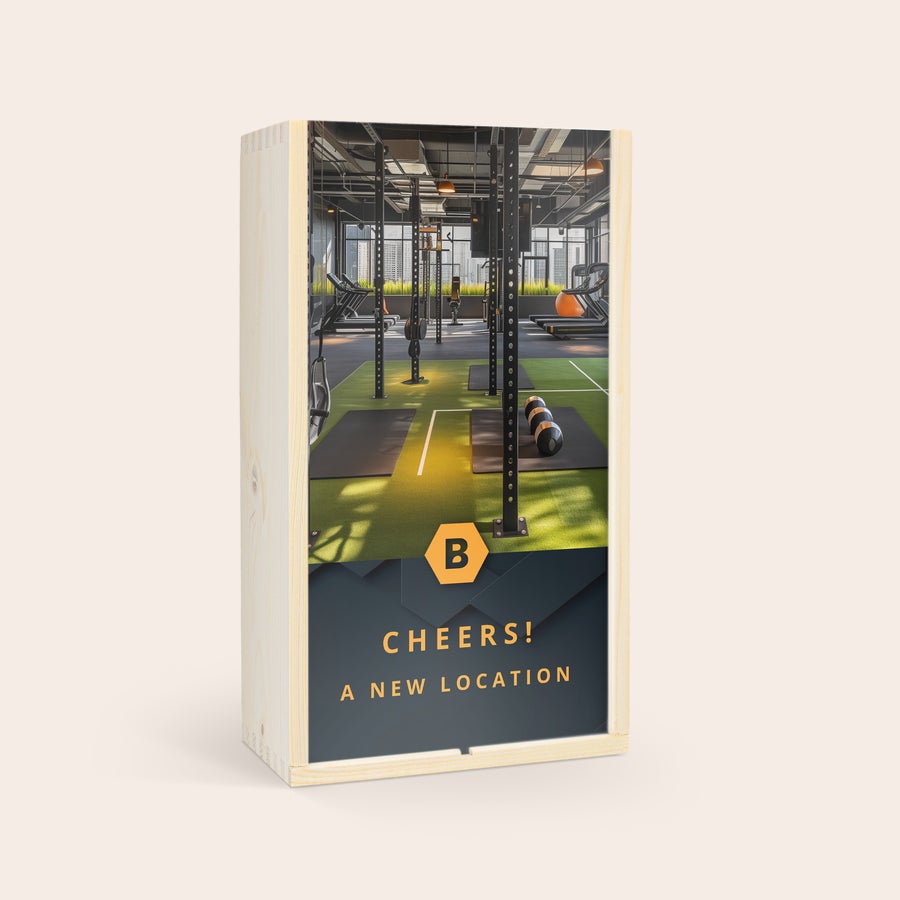 Jack Daniels Gentleman Jack Bourbon in kist personaliseren Houten kist bedrukt met foto van een sportschool, oranje logo met letter B en de tekst CHEERS! A NEW LOCATION.