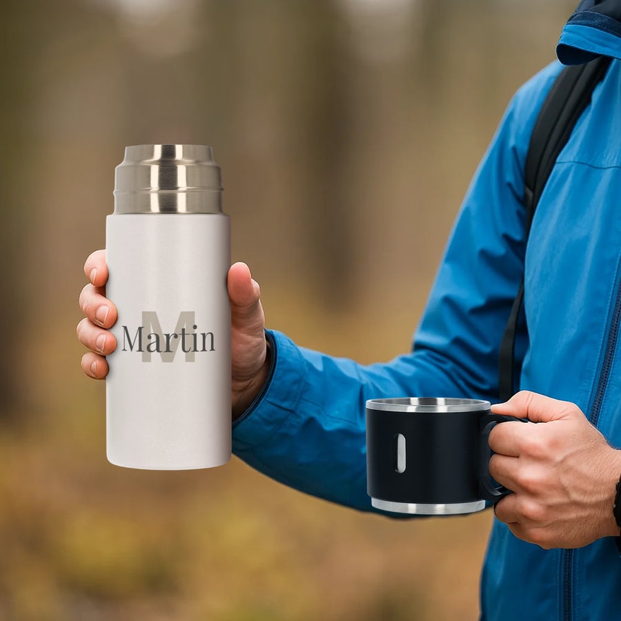 Petaca con taza - personalizada Termo personalizado blanco de 350 ml con nombre Martin impreso y taza negra en la mano de una persona.