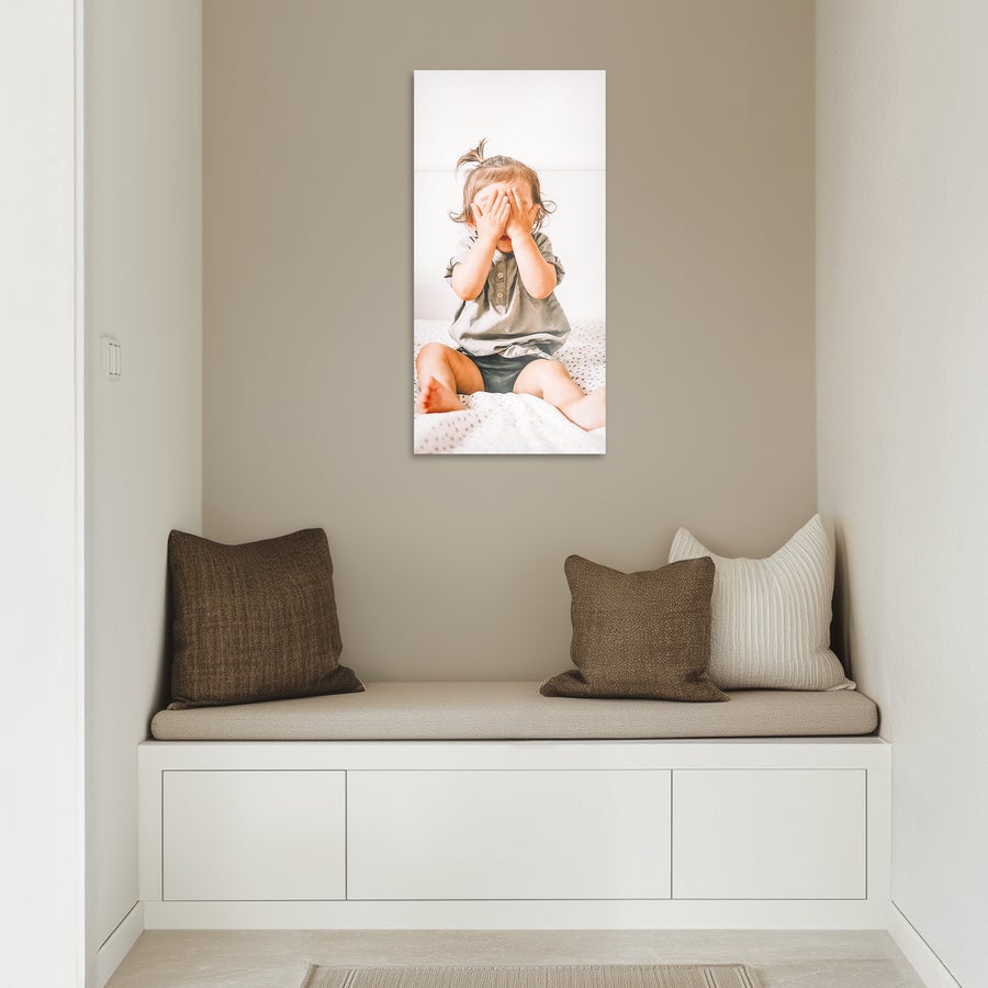 Foto auf Alu Fototafel hochformatig an einer hellen Wand mit Foto eines kleinen Kindes das sich die Hände vor das Gesicht hält bedruckt