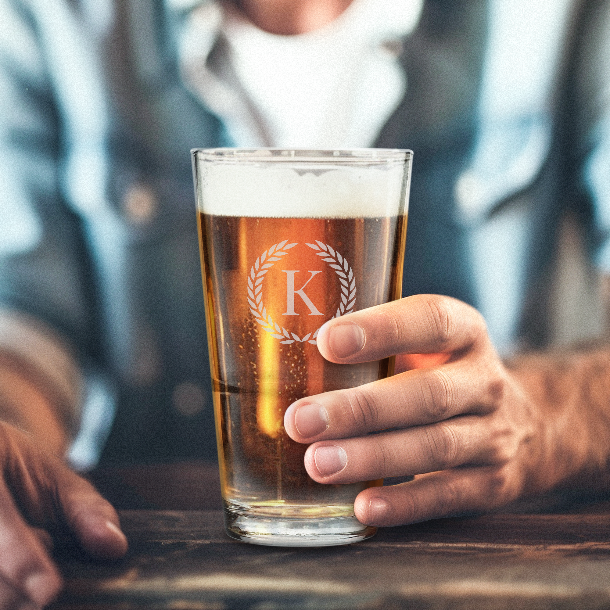 Een man houdt een gepersonaliseerd vaasje gevuld met bier vast, gegraveerd met de letter K en een lauwerkrans, om mee te proosten.