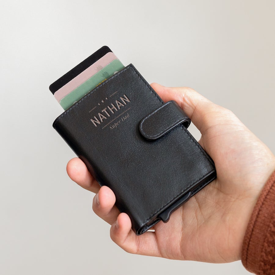 Portacarte con nome Mano che regge un portacarte bancario in pelle nero con carte e inciso "NATHAN Super Dad"