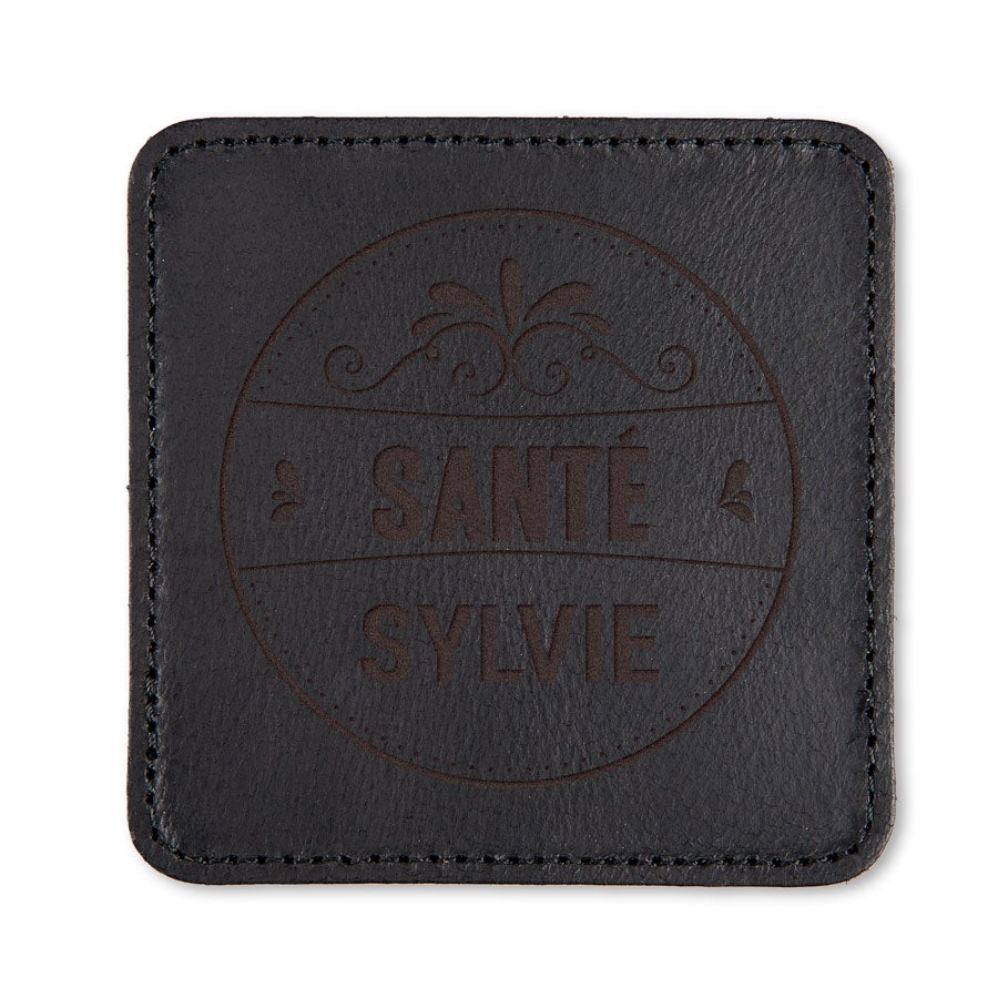 Sous-verre en cuir noir gravé avec un motif décoratif, texte Sante a Sylvie, un sous-verre en cuir gravé