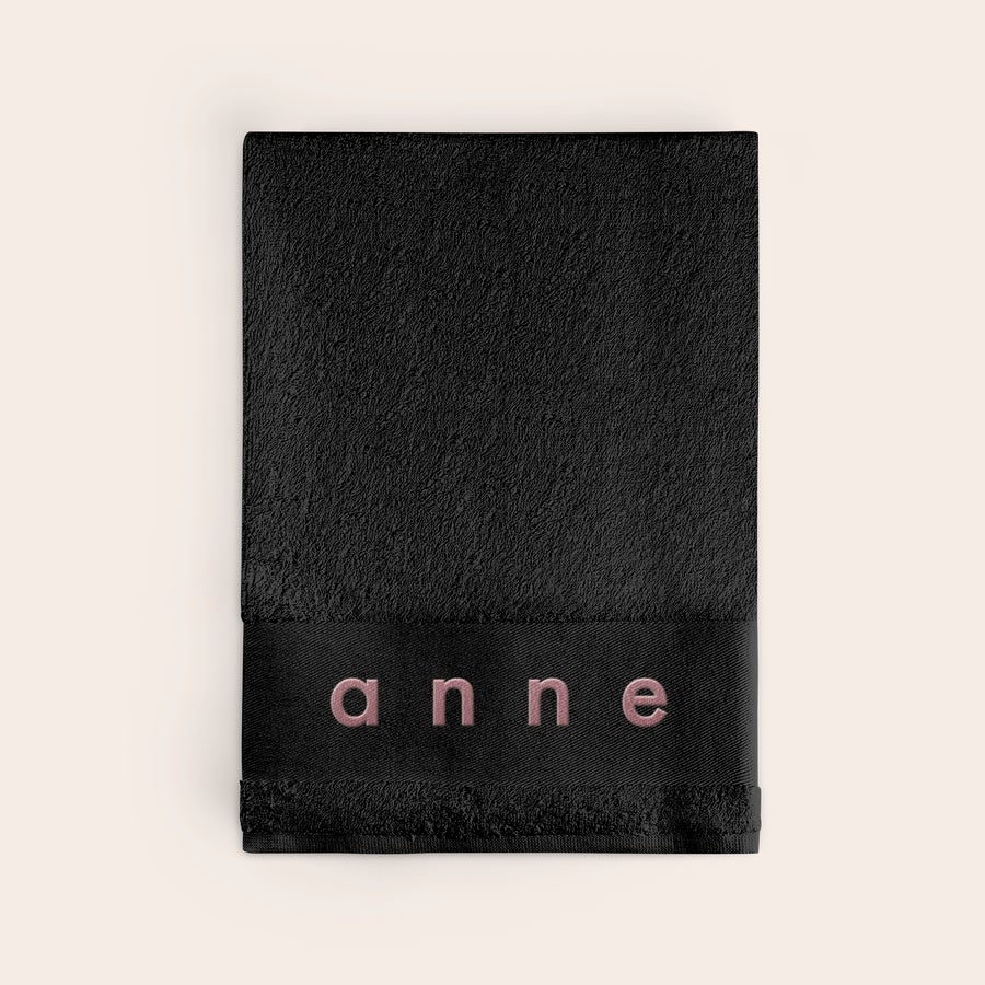 Bath towel with text Personalised black bath towel with the name "Anne" embroidered in pink thread, creating something special