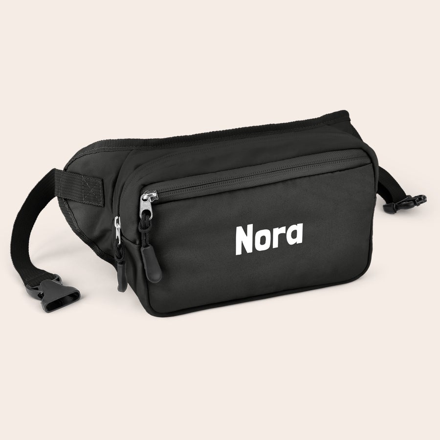 Personlig tilpasset rumpetaske Personlig svart rumpetaske med glidelås, trykket med navnet "Nora" i hvite bokstaver.