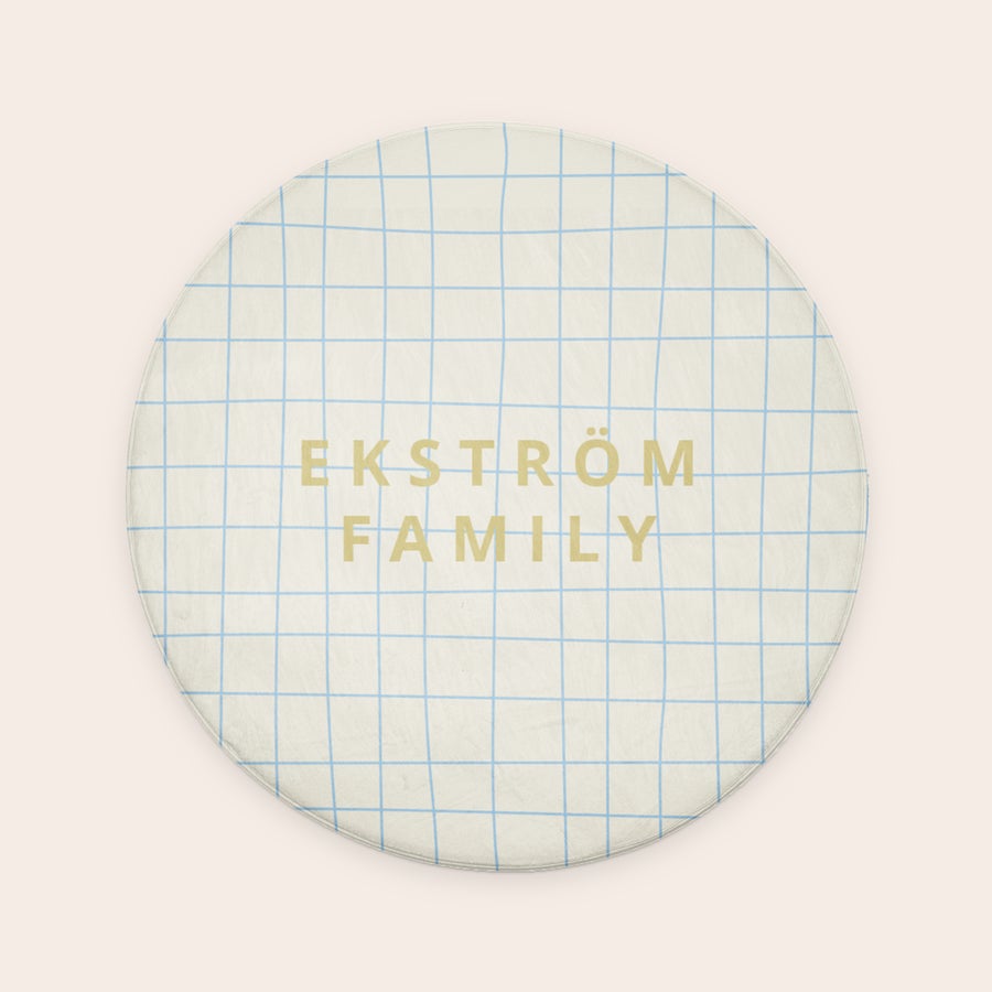 Personlig badrumsmatta - ø 70 cm Rund personlig badrumsmatta med ett blått rutmönster och namnet "EKSTRÖM FAMILY" tryckt i guld.