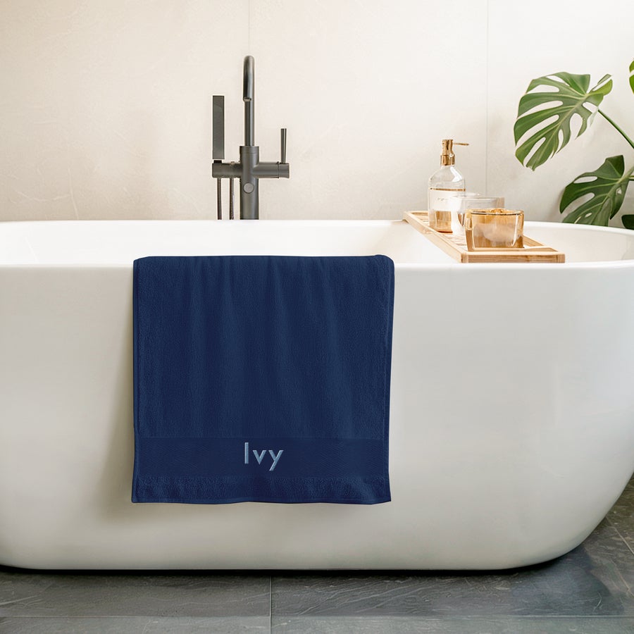 Towel with text Navy blue embroidered towel with the name Ivy in light blue stitching hanging over a white bathtub