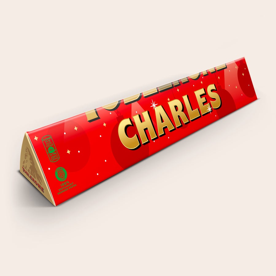 XXL Toblerone-suklaa nimellä Jättikokoinen Toblerone-patukka punaisella kääreellä, jossa on painettu kultainen nimi CHARLES. Tämä jättiyllätys on personoitavissa.