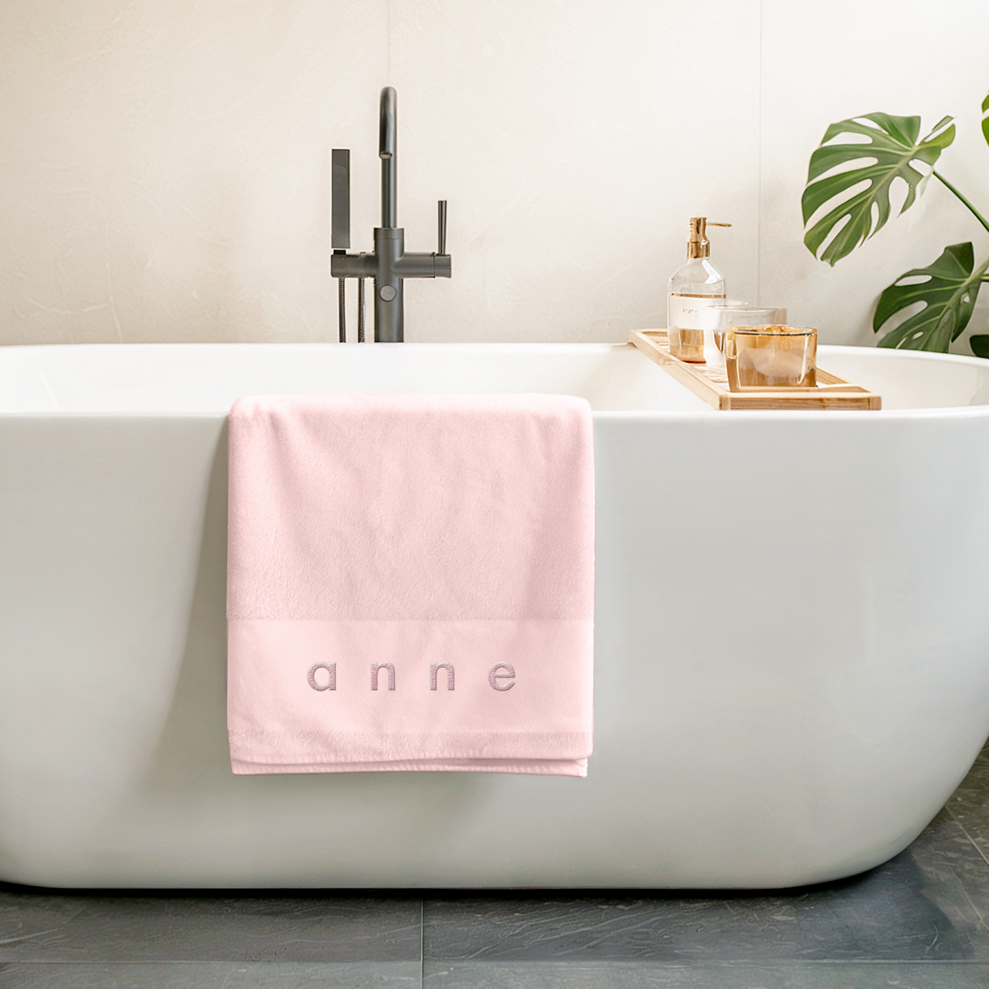 Serviette de bain rose avec un nom brodé personnalisable pour la plage, posée sur une baignoire blanche
