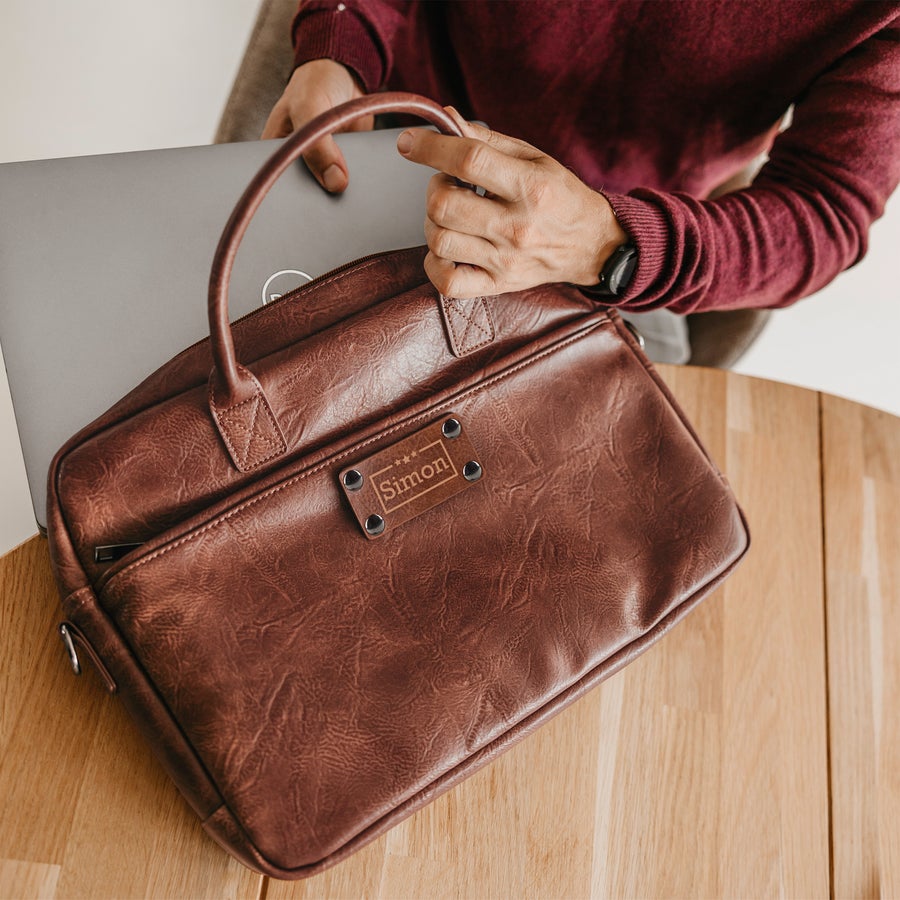 Personlig laptopväska i PU-läder Personlig laptopväska i brunt PU-läder med namnet Simon graverat på en etikett.