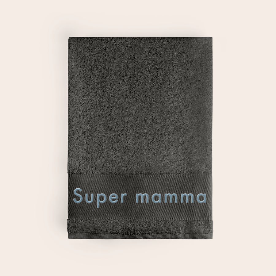 Handduk med Text Grå handduk i frotté, broderad med namnet "Super mamma" i ljusblått.