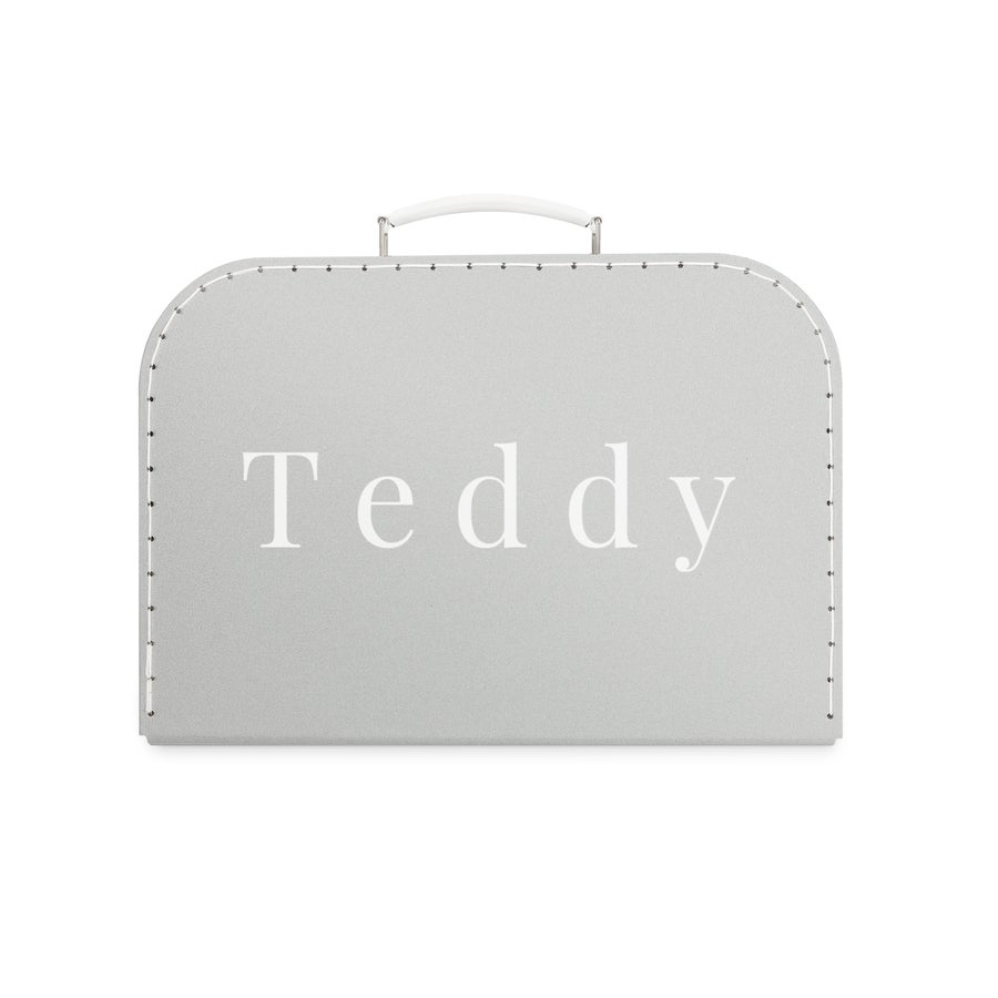 Valiză de jucărie personalizată Această frumoasă valiză de jucărie imprimată este detaliul perfect pentru camera oricărui copil. Valiză gri din carton, personalizată cu numele Teddy scris alb pe mijloc.