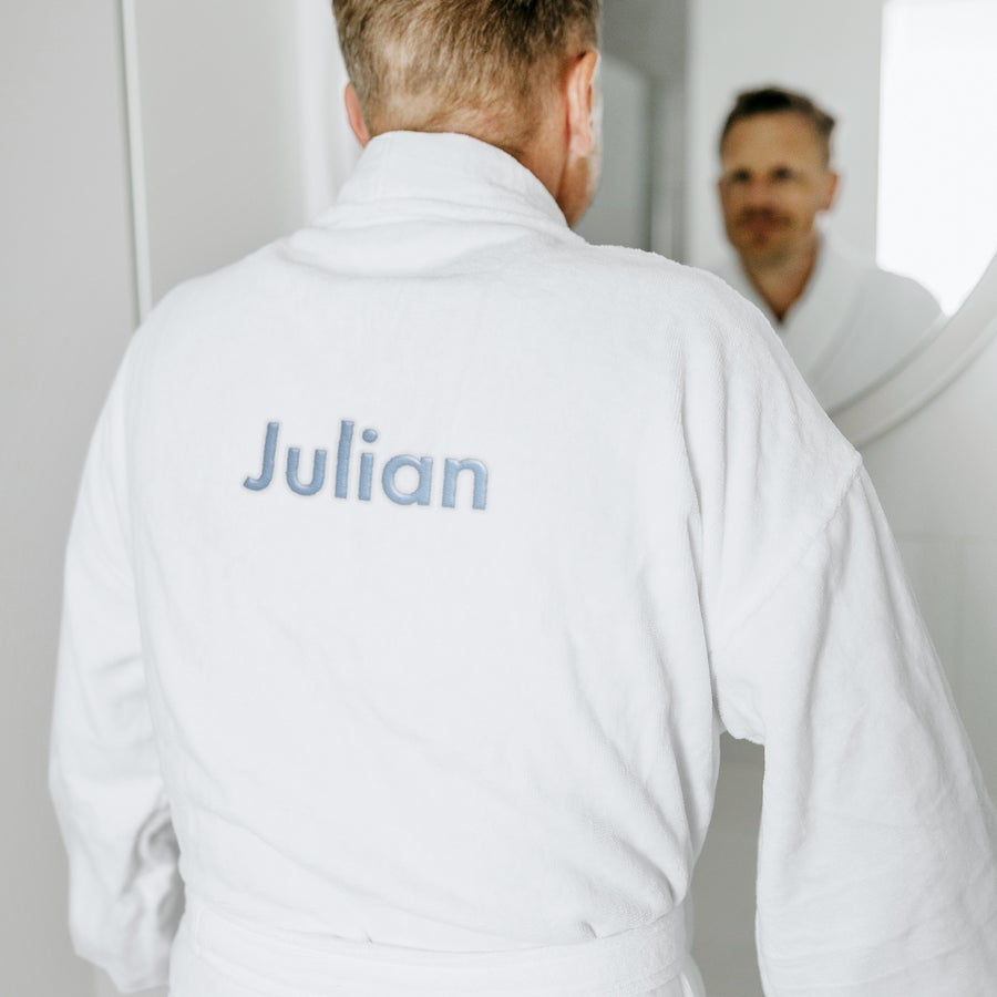 Bademantel Männer personalisiert Weißer Frottee-Bademantel, mit "Julian" in Hellblau auf dem Rücken bestickt, getragen von einem Mann von hinten.