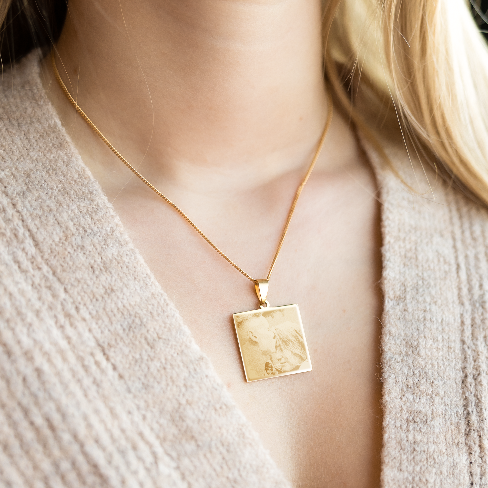 Goldfarbener quadratischer Anhänger mit Fotogravur eines Paares am Hals einer Frau