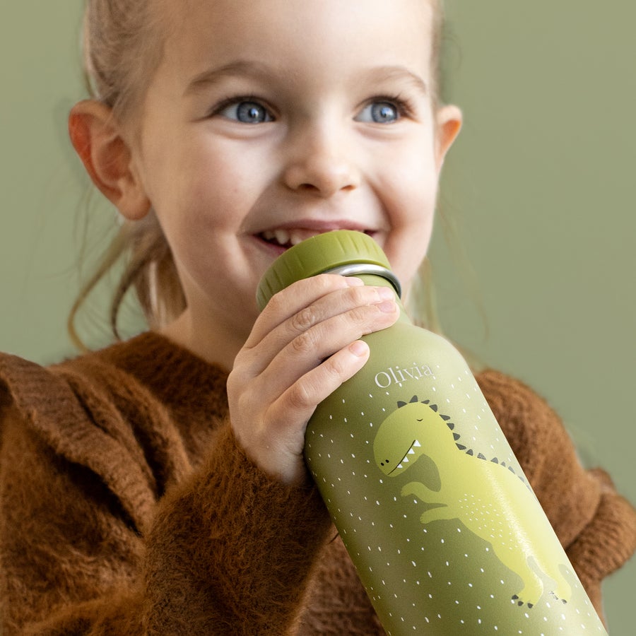 Trixie üveg állatok Személyre szabott Trixie állati vizes palack zöld színben, dinoszaurusz mintával és Olivia névvel lézergravírozva, melyet egy mosolygó kislány tart.