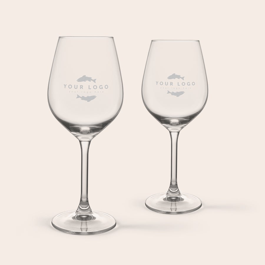 Set cadou vin și gustări - Alb - Pahare gravate Două pahare de vin alb personalizate, gravate cu logo-ul și textul "your logo here", parte dintr-un set cadou de vin și gustări.