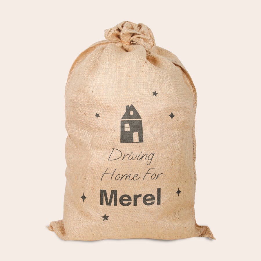 Jute kerstzak met naam bedrukt Jute kerstzak bedrukt met huisje, tekst "Driving Home For Merel" en sterren, gepersonaliseerde kerstcadeauverpakking