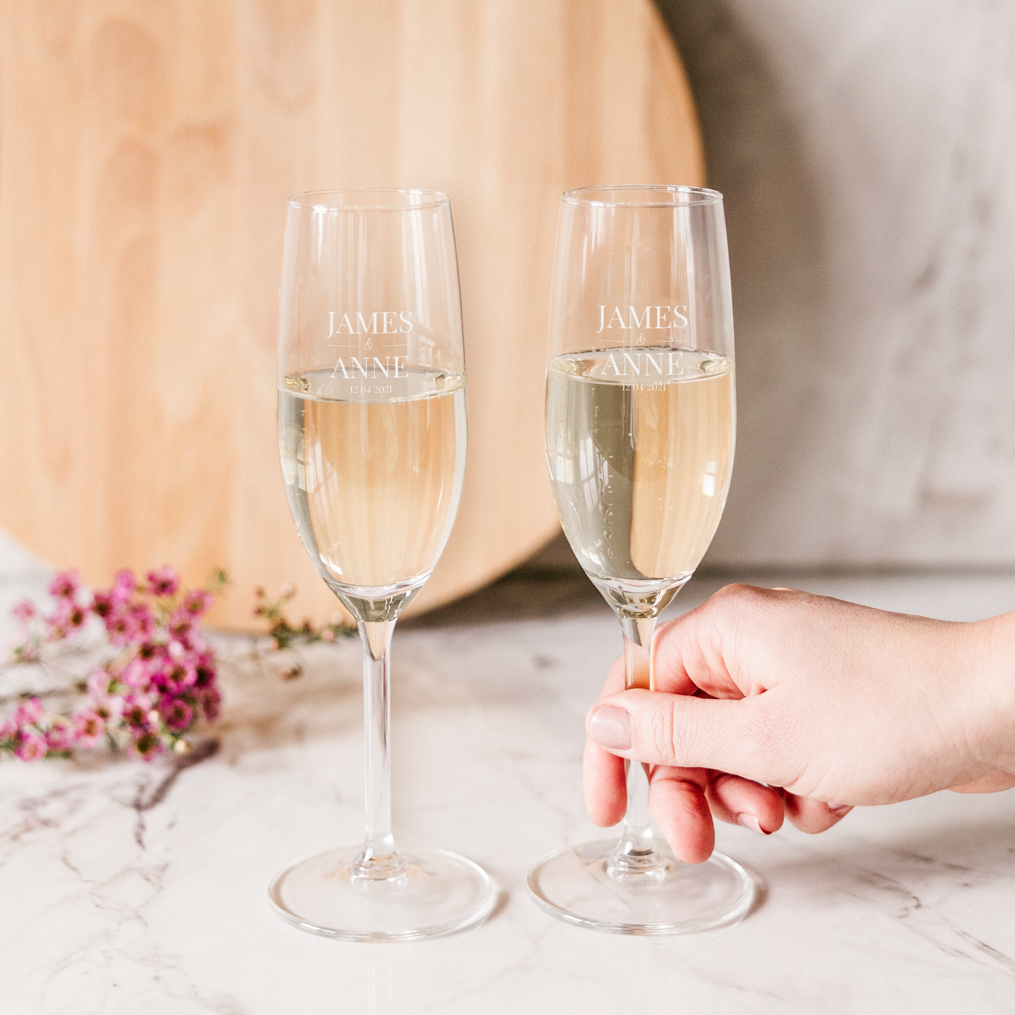 Zwei Sektgläser mit Namen "JAMES & ANNE" und dem Datum "12.04.2021" per Lasergravur individualisiert, gefüllt mit Sekt.