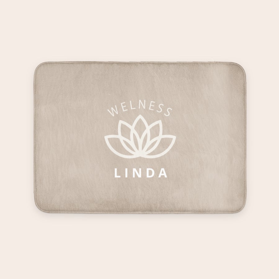 Personlig bademåtte - 70 x 50 cm En personlig bademåtte i beige med "Wellness" og et lotusblomst-logo over navnet "Linda", trykt i hvidt.