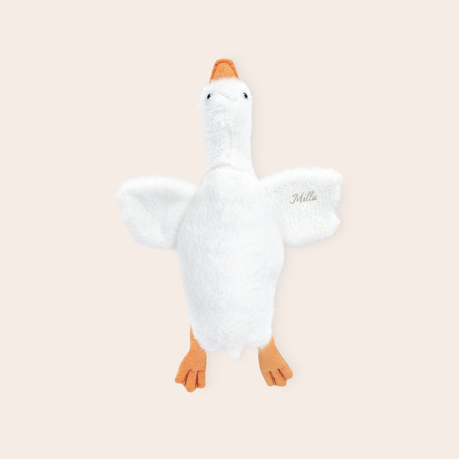 Gans Kuscheltier Personalisiert Weiße kuschelige Gans Plüschtier mit orangem Schnabel und Füßen, auf dem rechten Flügel ist der Name Milla gestickt, diese süße Kuschelgans kann es nicht abwarten mit deinem Mini zu kuscheln