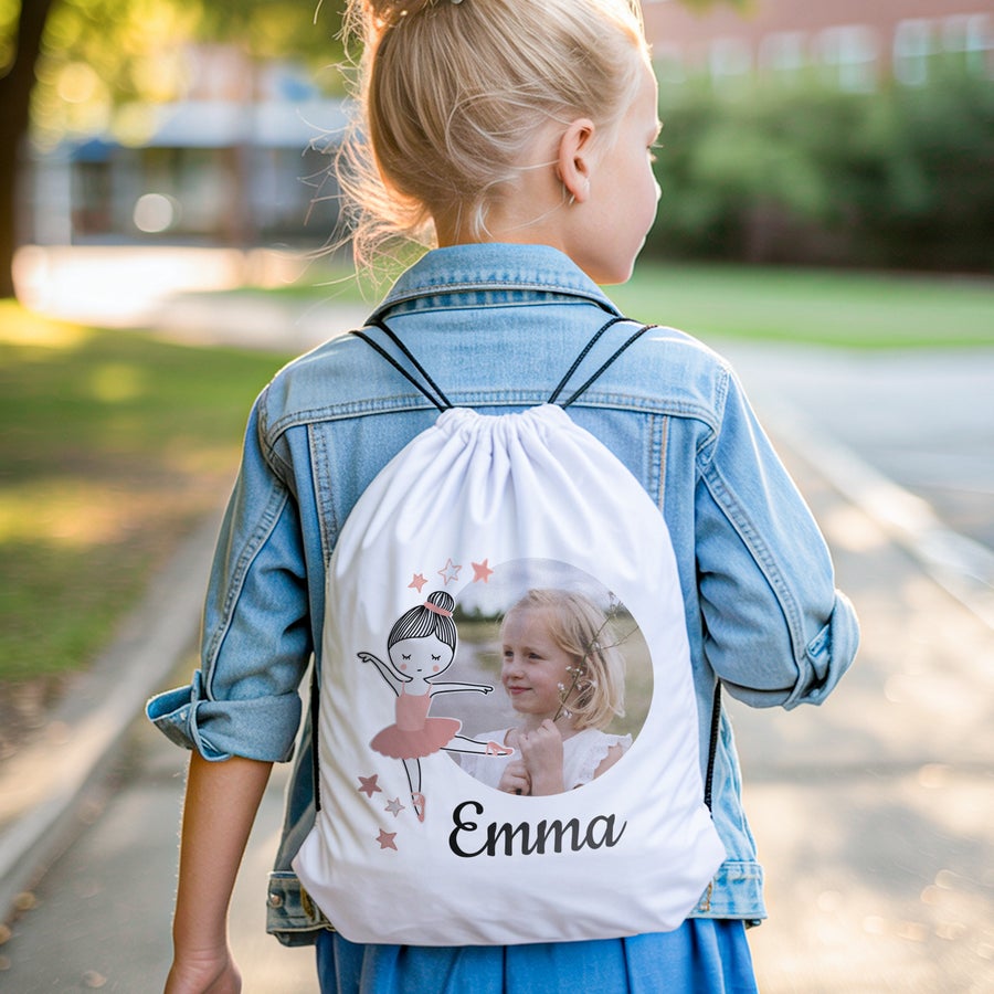 Gymtas bedrukken Een kind met gepersonaliseerde gymtas bedrukt met foto, naam 'Emma' en een ballerina figuur.