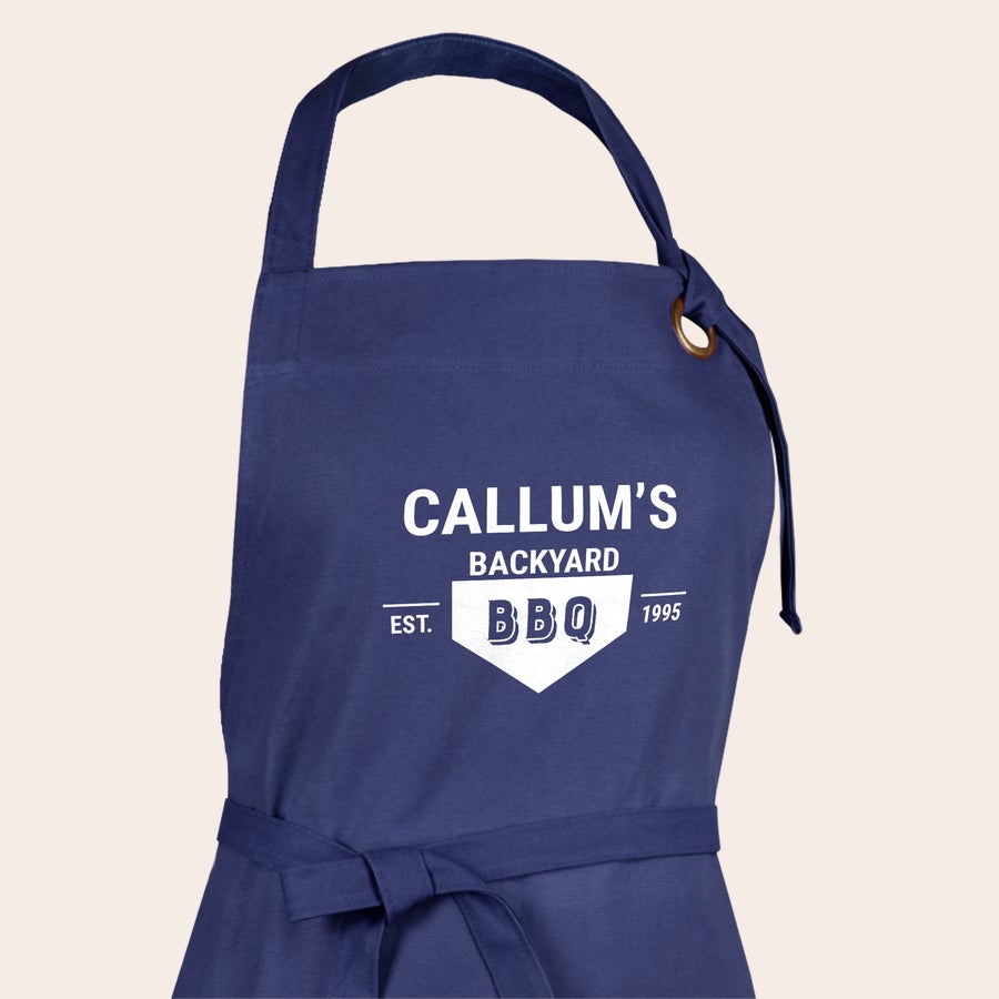 Delantal Delantal de cocina azul marino con estampado blanco "CALLUM'S BACKYARD BBQ EST. 1995"