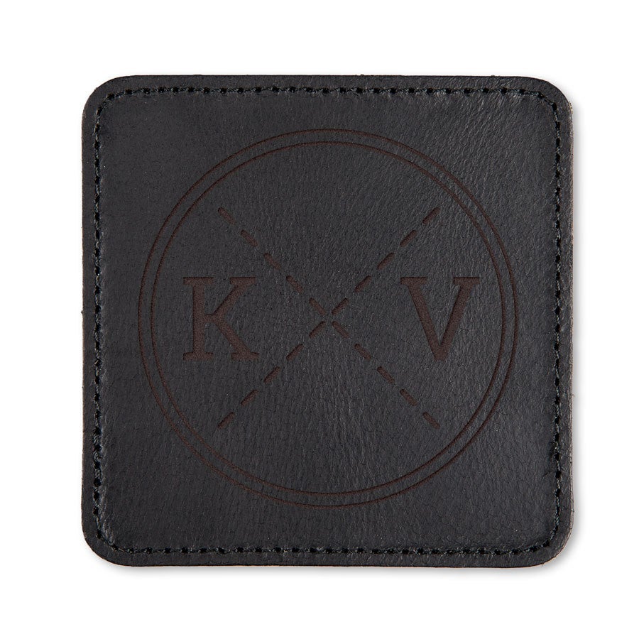 Set suport pahare personalizat Suport de pahar negru din piele, pătrat, gravat cu inițialele K și V, într-un design circular.