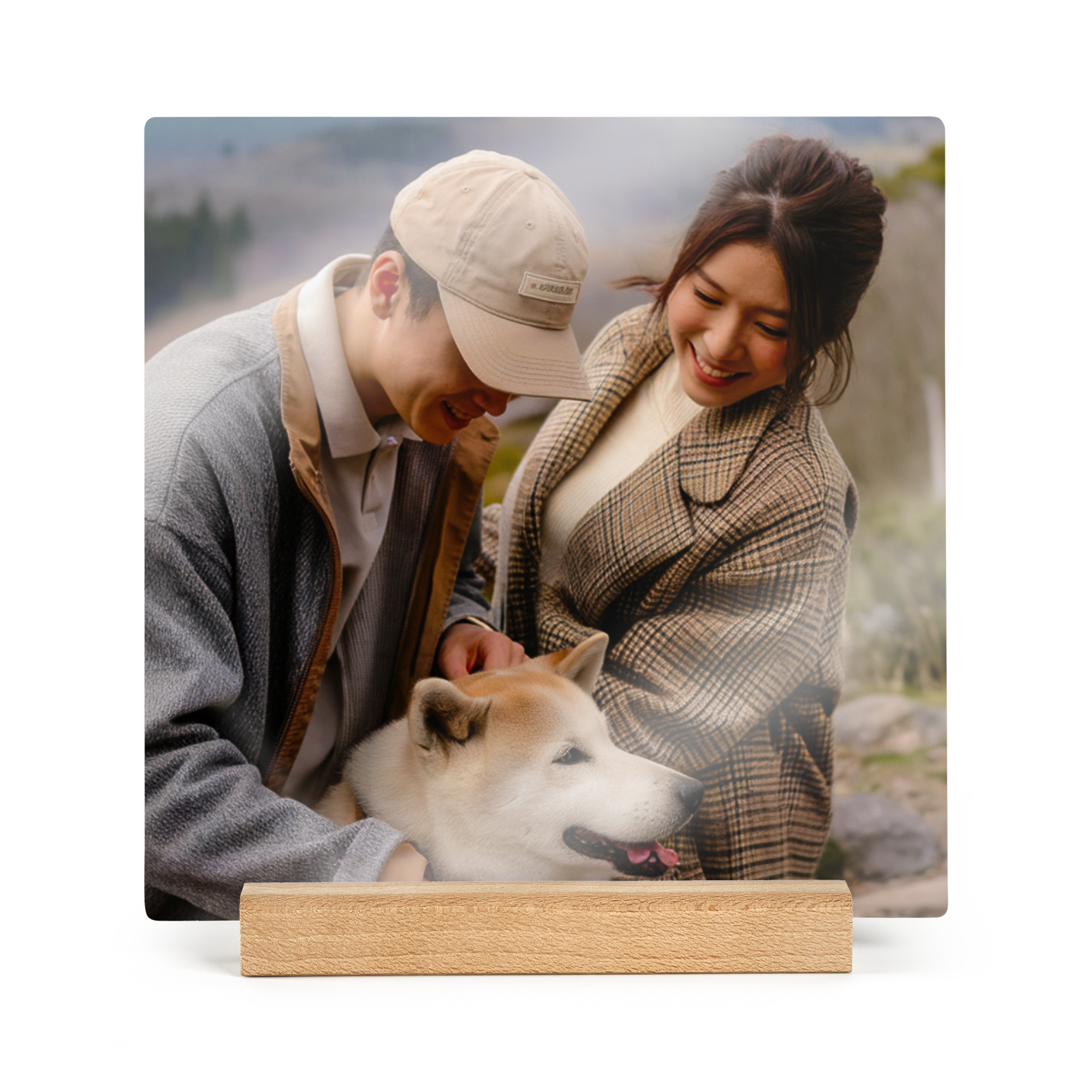 Eine quadratische Fotofliese aus Holz, bedruckt mit einem Foto von einem Paar, das einen Hund streichelt. Die quadratische Fotofliese steht auf einem Holzständer.