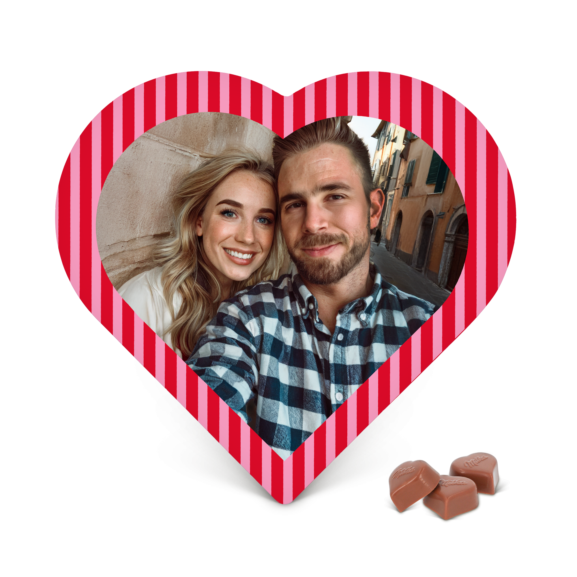 Cutie de ciocolată inimă personalizată Milka, cu o fotografie imprimată cuplu fericit și margini dungate roșii și roz. Trei praline Milka stau lângă cutie.