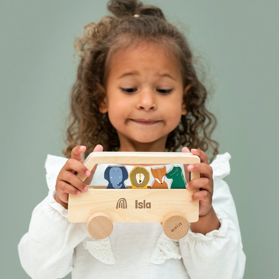 Puinen eläinbussi nimellä - Trixie Lapsi pitää käsin kaiverrettua puista eläinbussia nimellä Isla ja sateenkaarilogolla